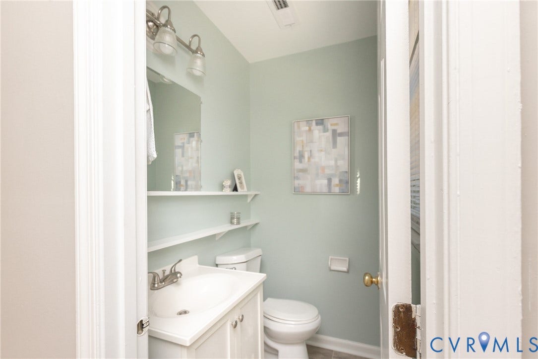 Bathroom featuring a white vanity with integrated sink, brushed nickel faucet, wall-mounted mirror, and two floating shelves