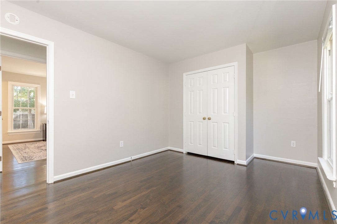 Dark wood-finish flooring, light neutral wall tones, white trim, white paneled bifold doors, and a double-hung window