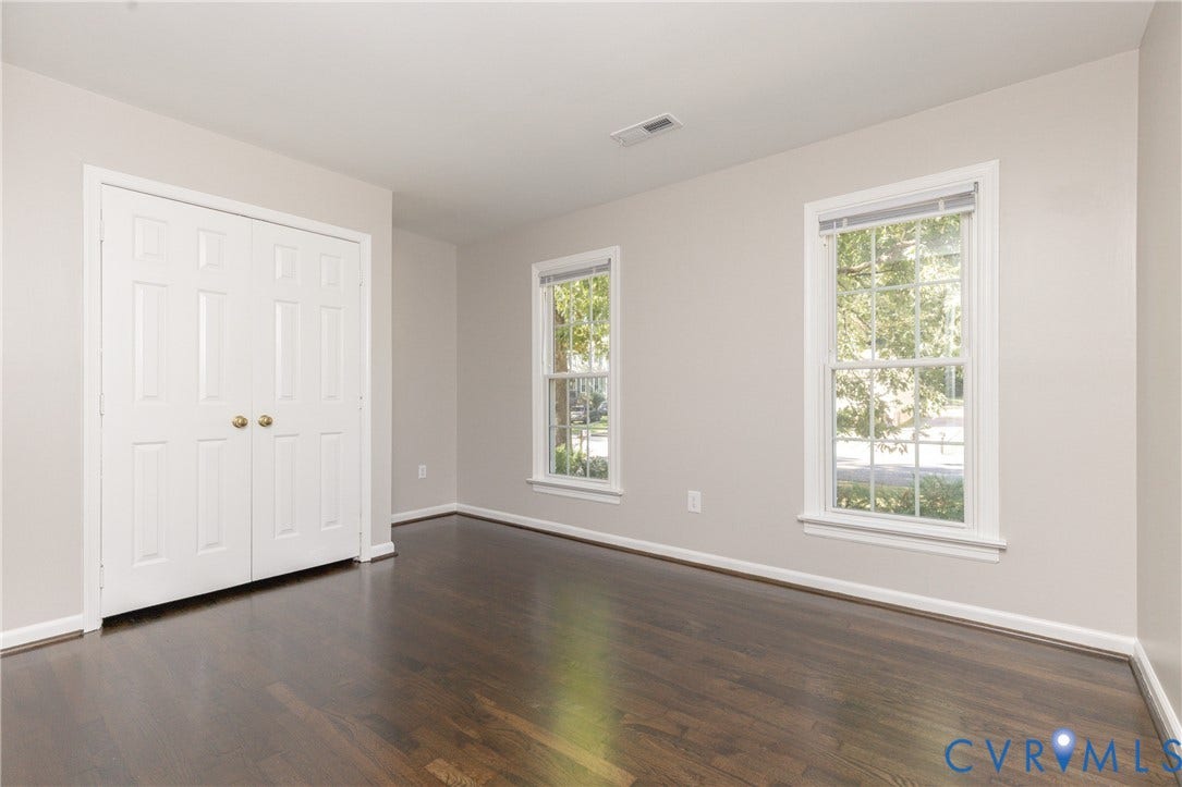 Dark wood-finish flooring, white bi-fold closet doors with brass hardware, and two large windows with white trim
