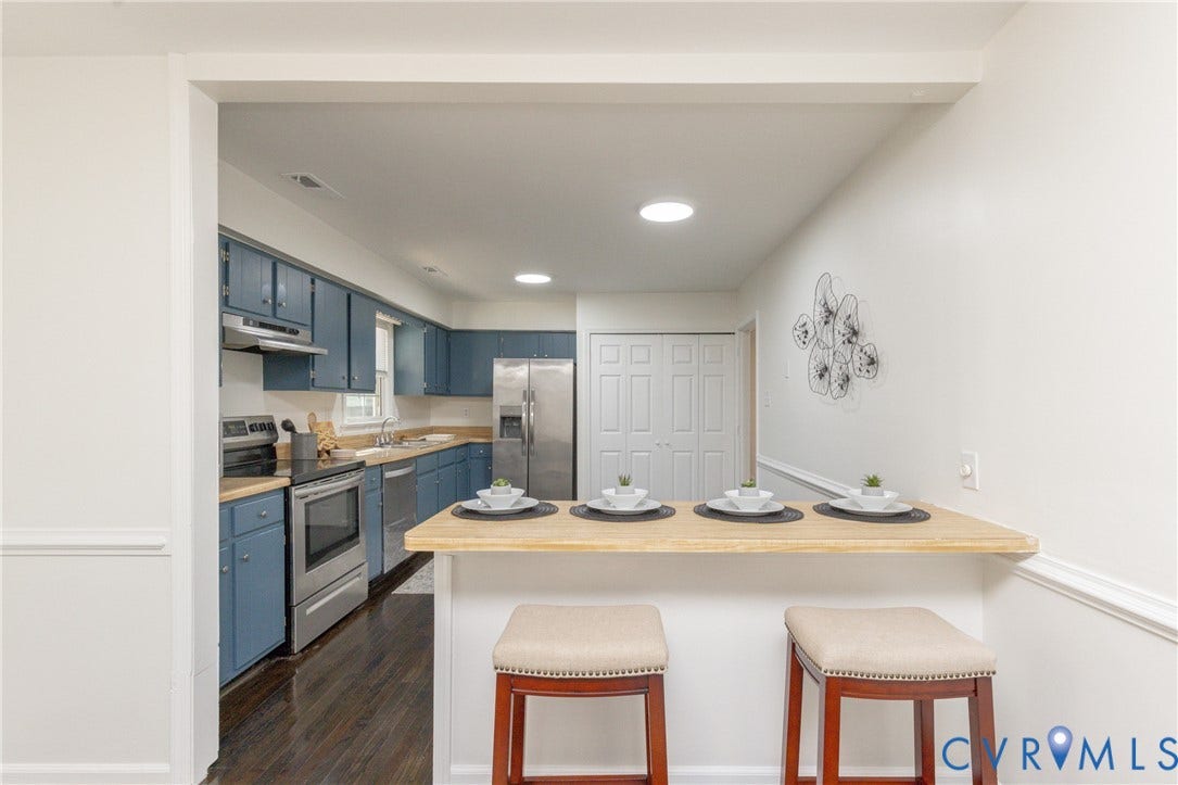 Kitchen featuring blue cabinetry, stainless steel appliances, dark wood-finish flooring, and a breakfast bar with a light-tone countertop