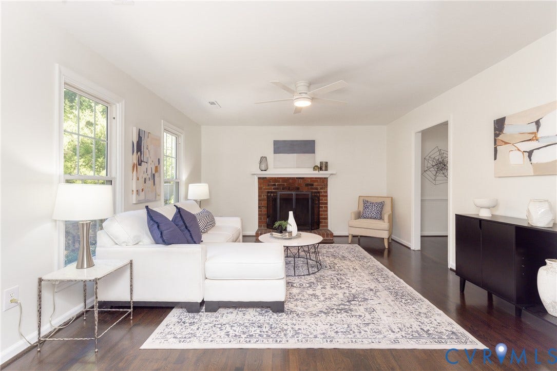 Brick fireplace with a white mantel, dark wood-finish flooring, white walls, and a ceiling fan