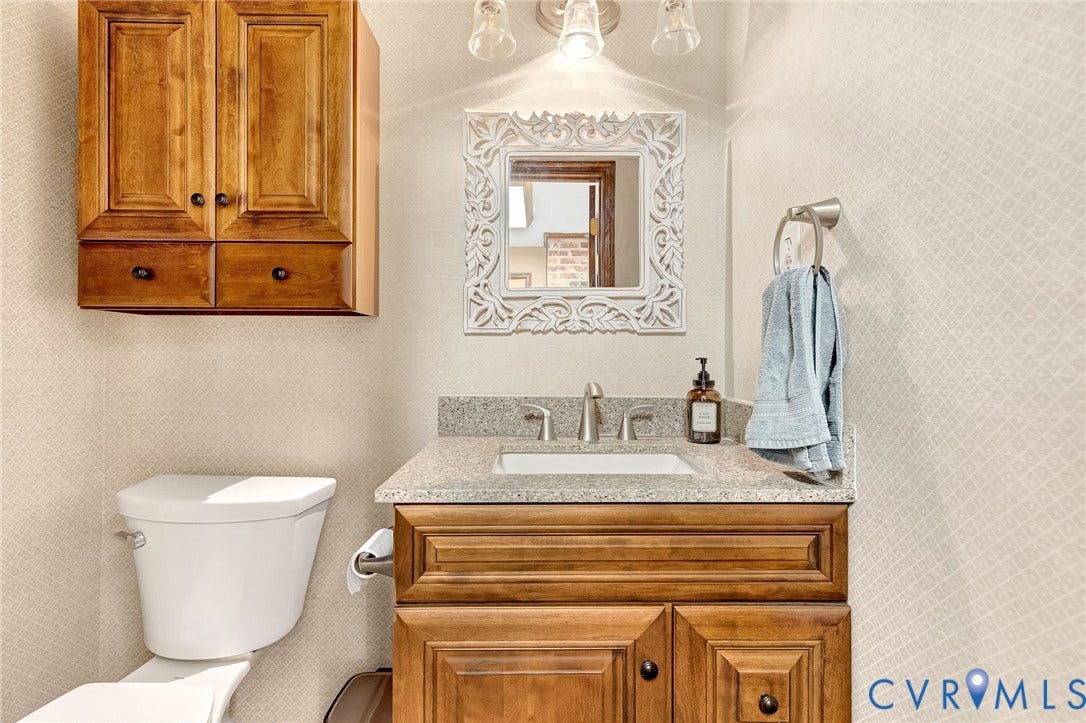11410 Driscoll Road, Chester, VA 23831 Wood-finish cabinetry, neutral stone-composite countertop with an integrated rectangular sink, three-light fixture, and textured wall finish