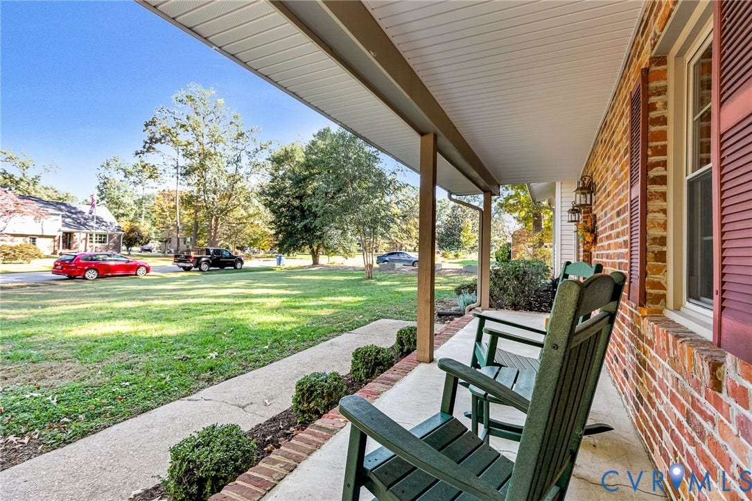 11410 Driscoll Road, Chester, VA 23831 Covered front porch featuring a brick exterior, red louvered shutters, concrete flooring, and decorative wall-mounted lanterns