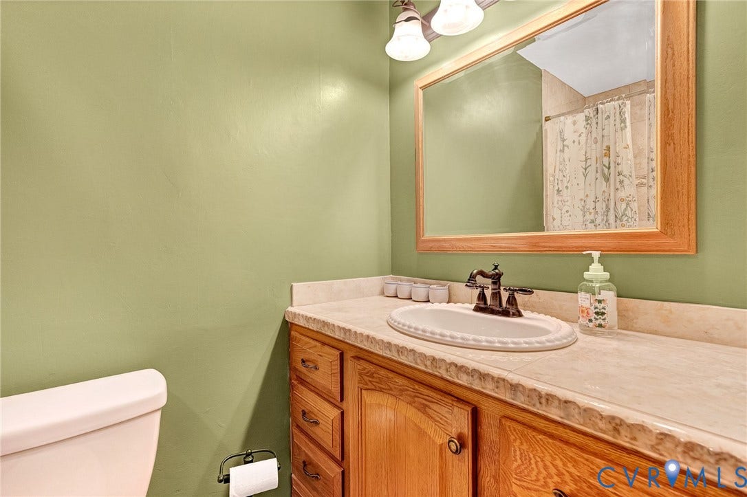11410 Driscoll Road, Chester, VA 23831 Bathroom vanity featuring wooden cabinetry, an integrated stone-finish countertop with a drop-in sink, oil-rubbed bronze faucet, and a large framed wall mirror