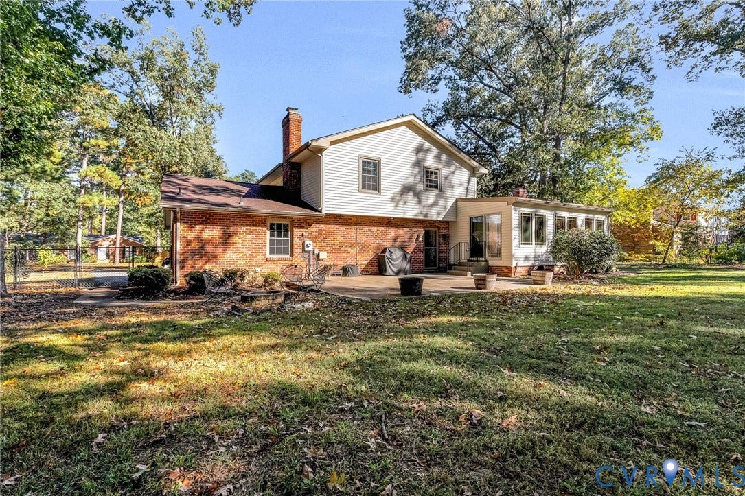 11410 Driscoll Road, Chester, VA 23831 Exterior elevation featuring brick and light-colored siding, masonry chimney, concrete rear patio, and mature trees on a level lot