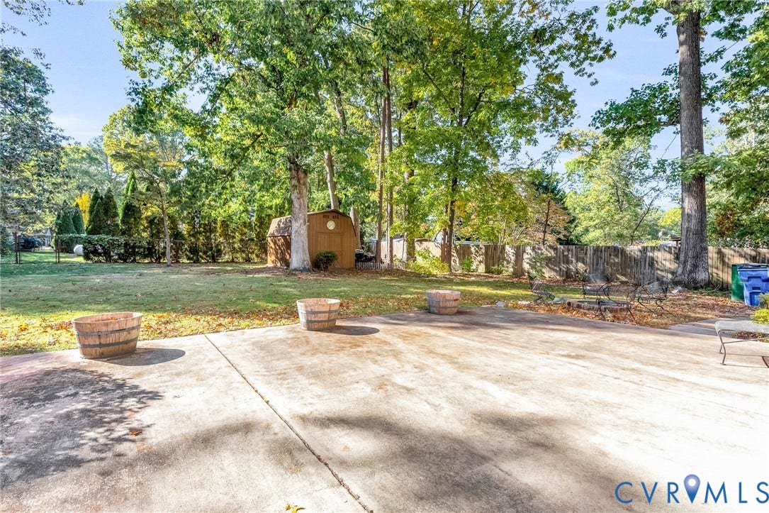 11410 Driscoll Road, Chester, VA 23831 Expansive backyard featuring a concrete patio, mature trees, and a detached storage shed enclosed by wood fencing