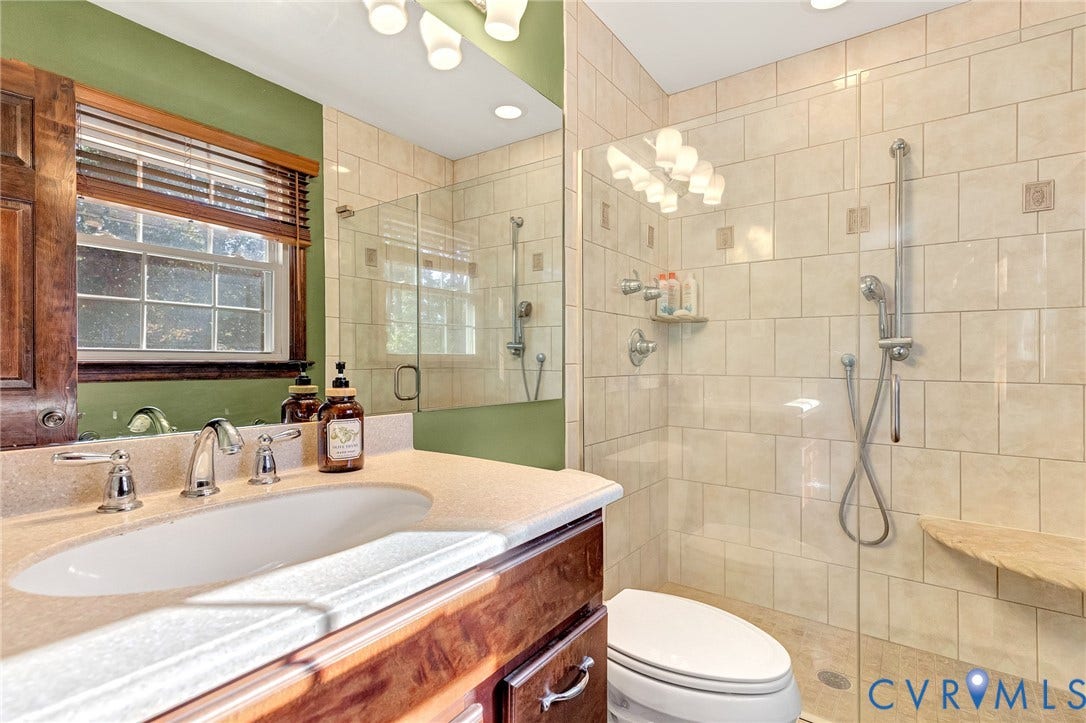 11410 Driscoll Road, Chester, VA 23831 Bathroom featuring a wood-finish vanity with an integrated sink, polished chrome faucet, large frameless glass-enclosed shower with tile surround, built-in corner shower bench, and adjustable handheld shower head