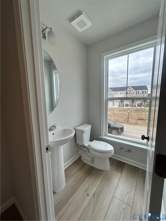 Pedestal sink with chrome faucet, round wall mirror, wood-finish flooring, and white window trim