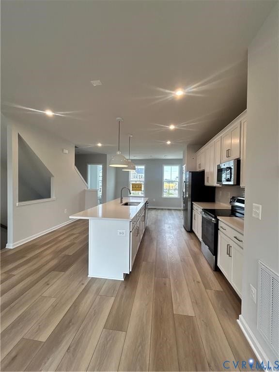 Wood-finish flooring throughout, kitchen island with built-in sink, stainless steel appliances, white cabinetry, and recessed lighting