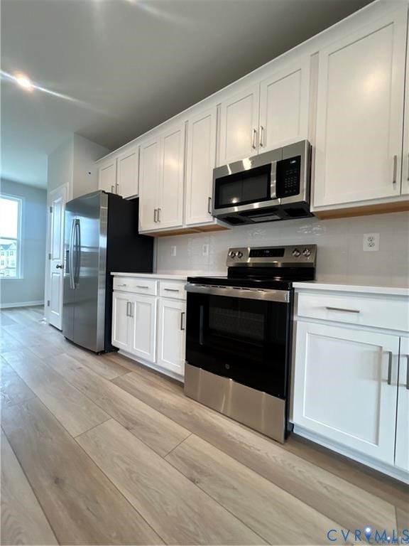 White cabinetry with brushed nickel hardware, stainless steel appliances, light-toned wood-finish flooring, and light-colored countertops