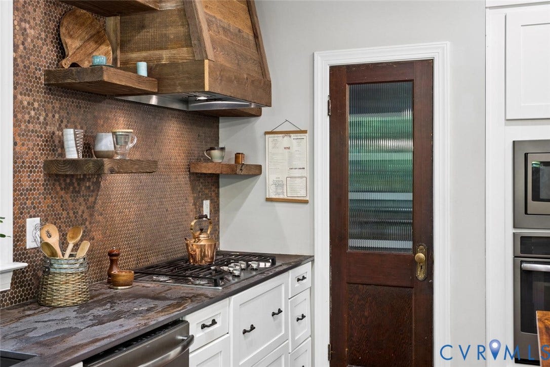 9013 Old Holly Road, Southhampton, Richmond, VA 23235 Copper penny tile backsplash, wood-finish floating shelves, wood-finish range hood, dark stone countertop, and white cabinetry with dark hardware