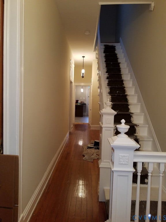 Hardwood flooring extending through the hallway, white painted stair railing with decorative newel posts, and recessed ceiling lighting