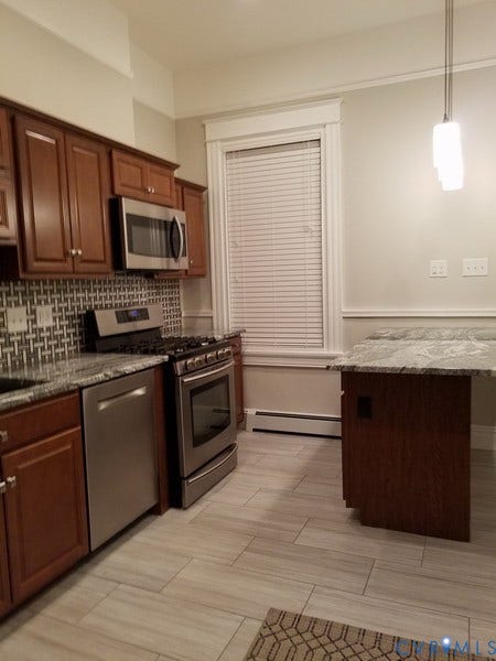 Kitchen featuring wood cabinetry, stainless steel appliances, patterned tile backsplash, and light-toned tile flooring