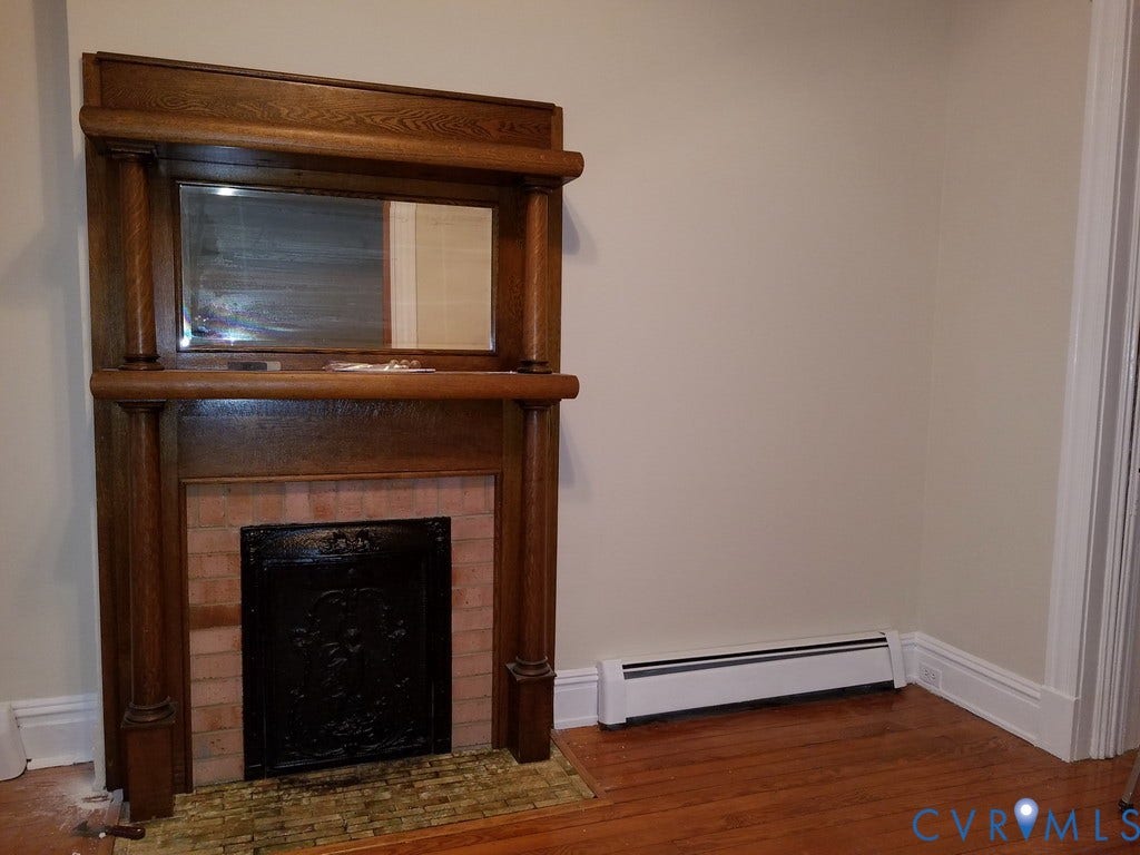 Wood-finish flooring, white baseboard trim, and a decorative fireplace with a wood mantle and brick surround