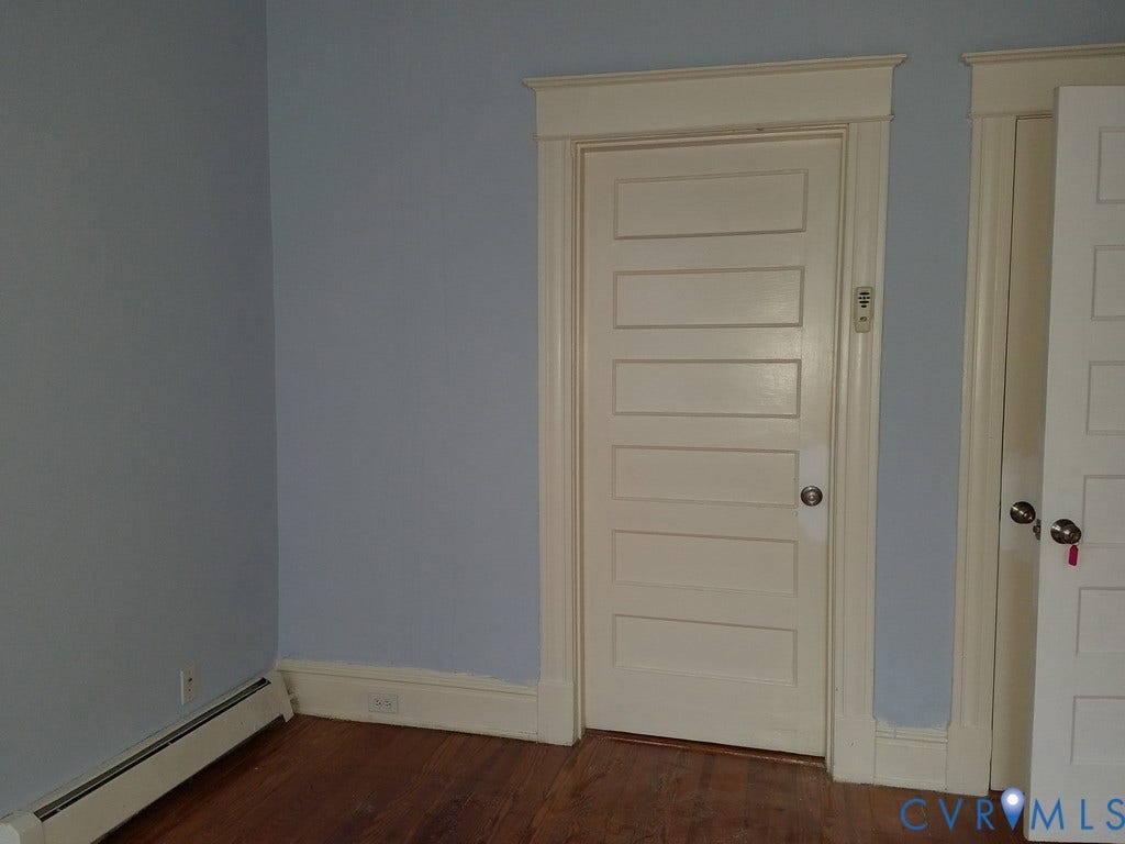Wood-finish flooring with light blue wall paint, white trim, and a paneled door
