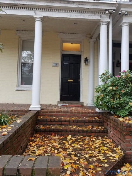 Brick steps with retaining walls, black paneled door with transom, and white architectural columns