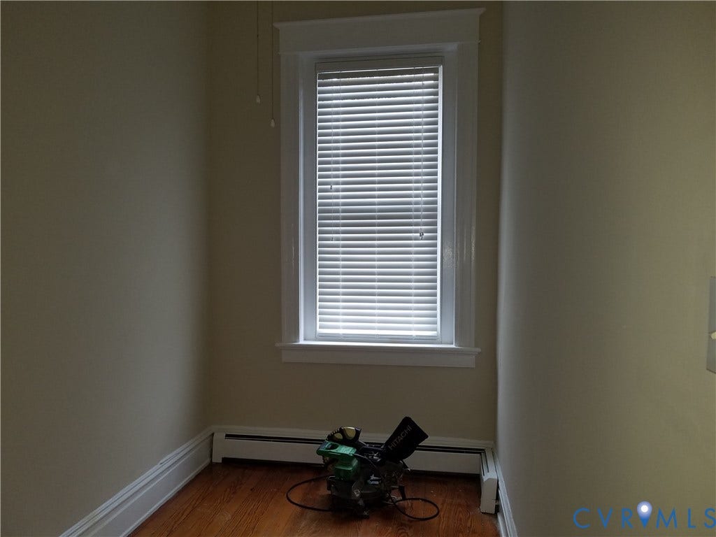 Wood-finish flooring, single window with blinds, white trim, and baseboard heating