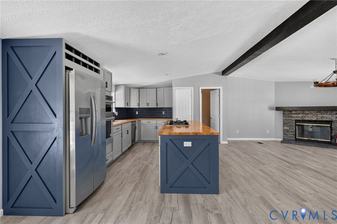 8211 Brills Road, Dinwiddie, VA 23872 Open-concept living space with wood-finish flooring, a stone-clad fireplace, and a vaulted ceiling with an exposed beam