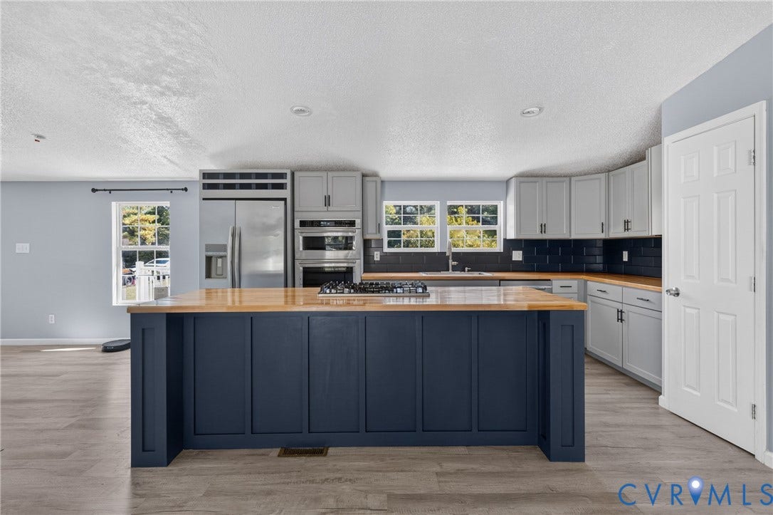 8211 Brills Road, Dinwiddie, VA 23872 Central island with wood-finish countertop, stainless steel appliances, light gray cabinetry, dark subway tile backsplash, and wood-finish flooring