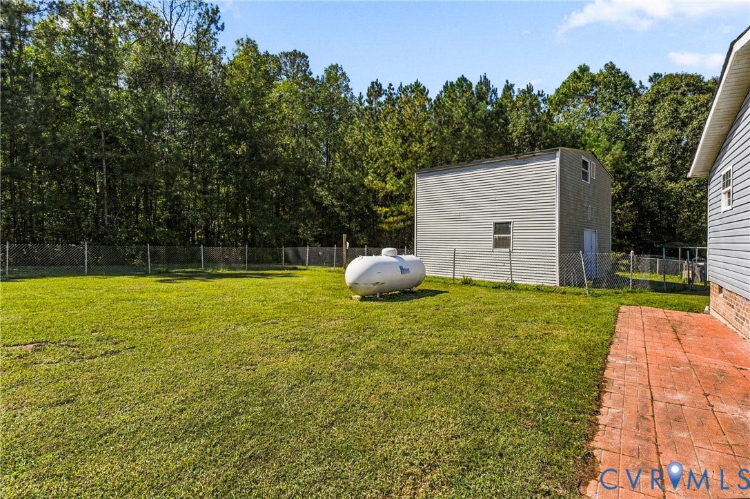 8211 Brills Road, Dinwiddie, VA 23872 Expansive grassy yard with chain-link fencing, mature trees, a two-story outbuilding, and a red brick pathway