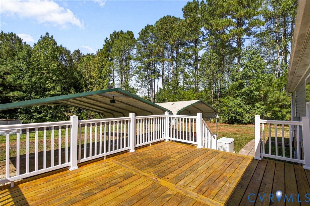 8211 Brills Road, Dinwiddie, VA 23872 Wood-finish deck with white railings, two covered carports, and mature trees