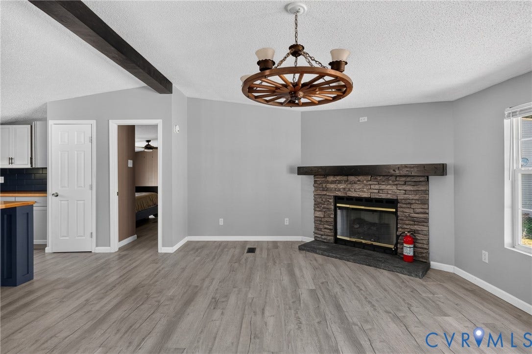 8211 Brills Road, Dinwiddie, VA 23872 Vaulted ceiling with exposed beam, stone-faced fireplace with hearth, wood-finish flooring, and wagon wheel-style chandelier