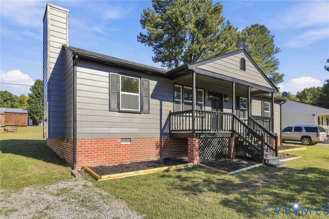 5113 Olympic Lane, North Dinwiddie, VA 23803 Single-story residence featuring horizontal siding, brick foundation, a covered front porch with dark railings, and an exterior chimney