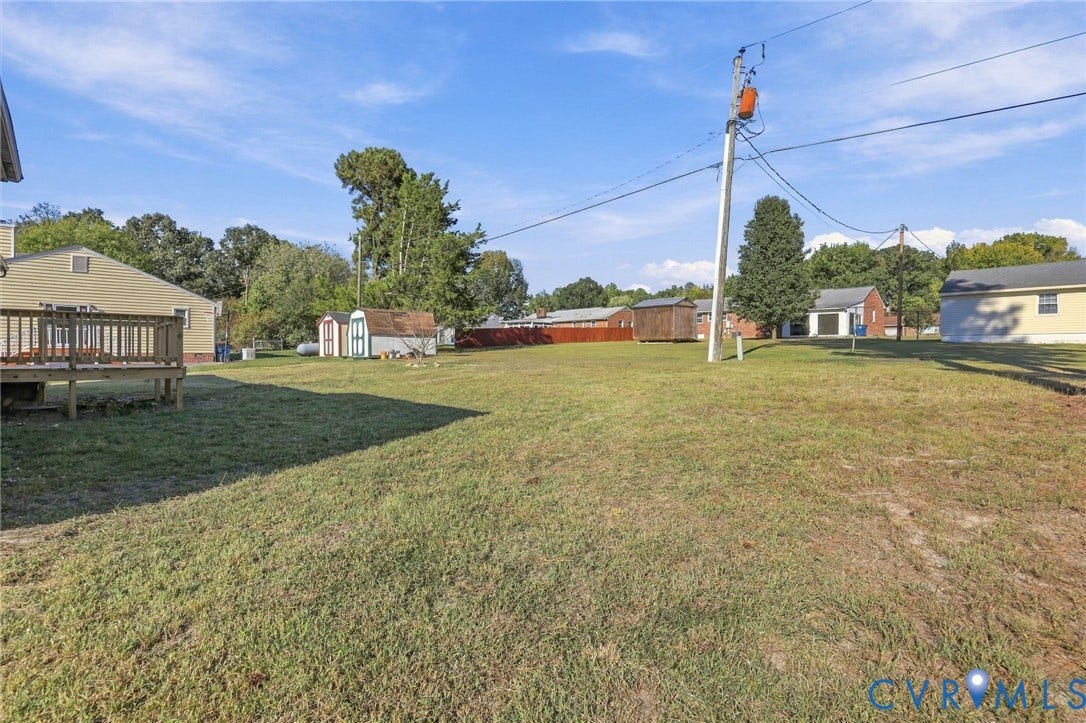 5113 Olympic Lane, North Dinwiddie, VA 23803 Expansive grassy yard with a wooden deck, two sheds, and a red privacy fence