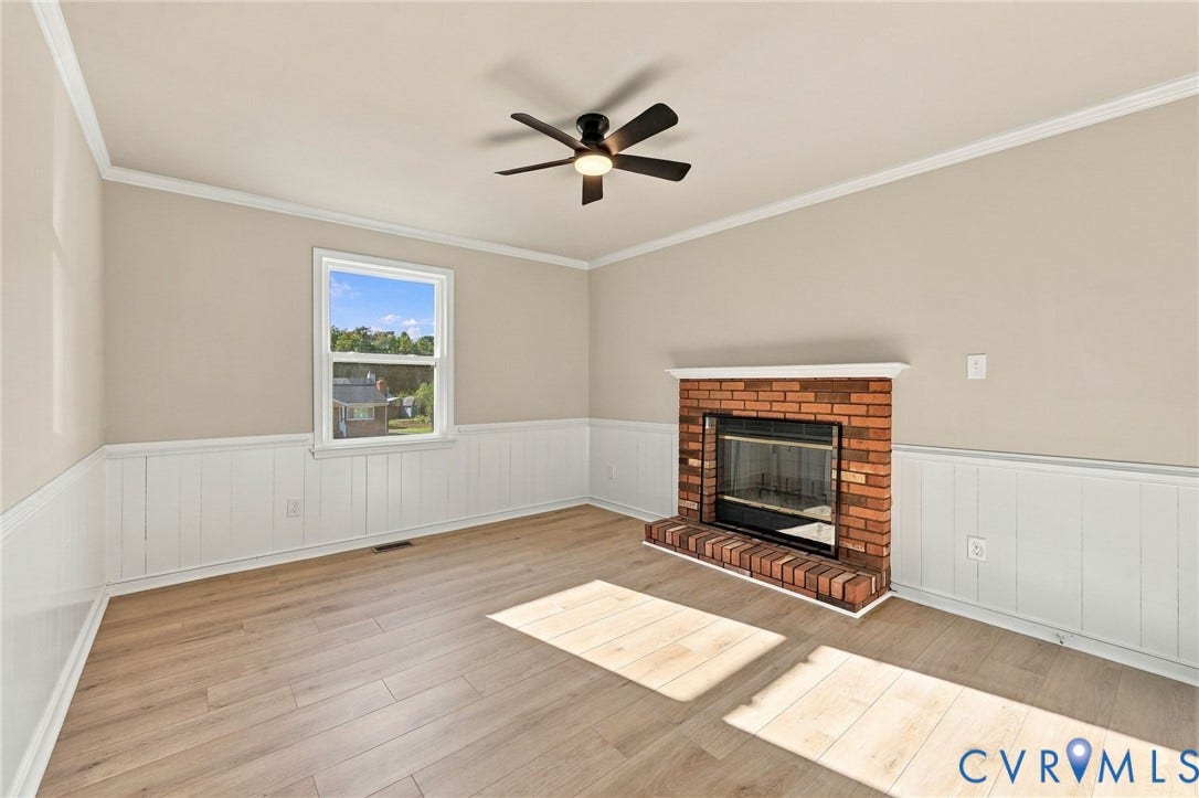 5113 Olympic Lane, North Dinwiddie, VA 23803 Brick fireplace with a white mantel, wood-finish flooring, white wainscoting, and a ceiling fan with integrated lighting