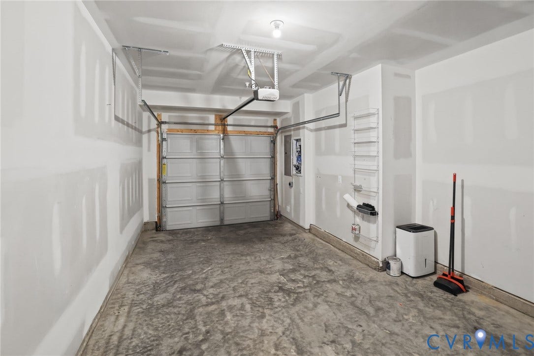 597 Weaver Brook Walk, #B, Richmond, VA 23233 Single-car garage featuring a concrete floor, finished drywall, an overhead sectional garage door, and a built-in wall-mounted shelving unit