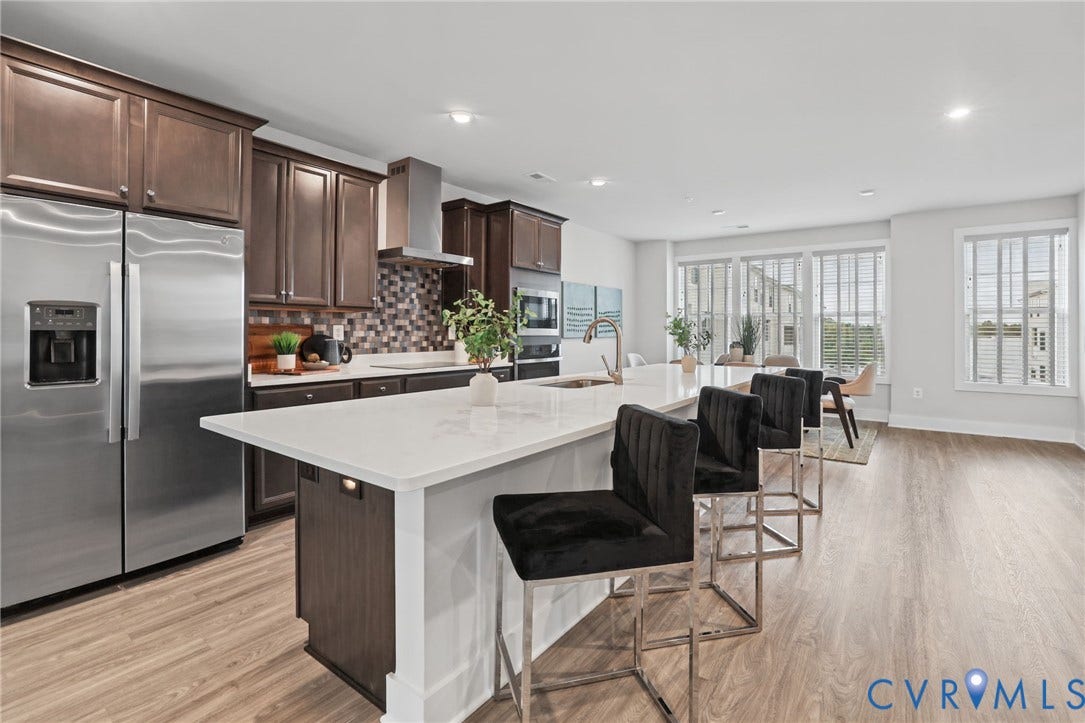 597 Weaver Brook Walk, #B, Richmond, VA 23233 Kitchen featuring dark wood cabinetry, a central island with a stone countertop, a tile backsplash, stainless steel appliances, and wood-finish flooring