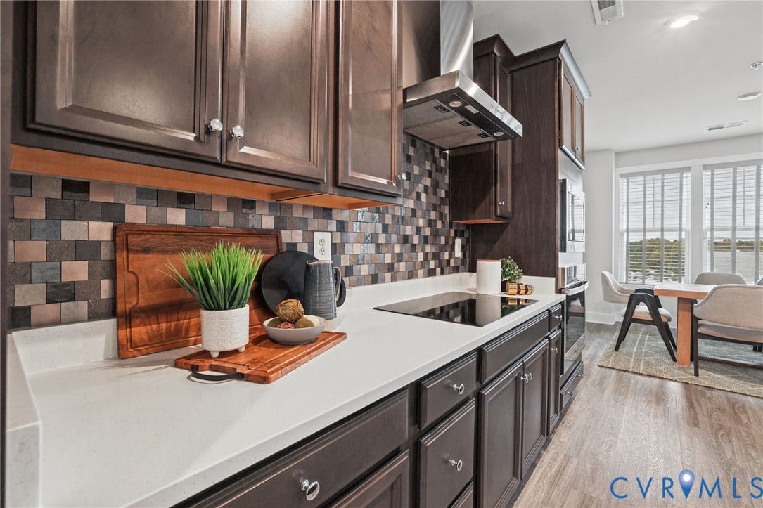 597 Weaver Brook Walk, #B, Richmond, VA 23233 Kitchen featuring dark cabinetry, solid-surface countertops, mosaic tile backsplash, stainless steel range hood, and wood-finish flooring