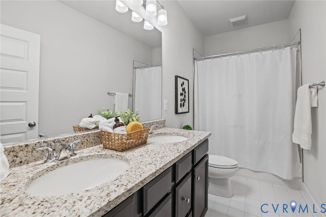 597 Weaver Brook Walk, #B, Richmond, VA 23233 Bathroom featuring a double-sink vanity with stone-surfaced countertops, dark cabinetry, polished chrome fixtures, and a shower-tub combination with a white surround