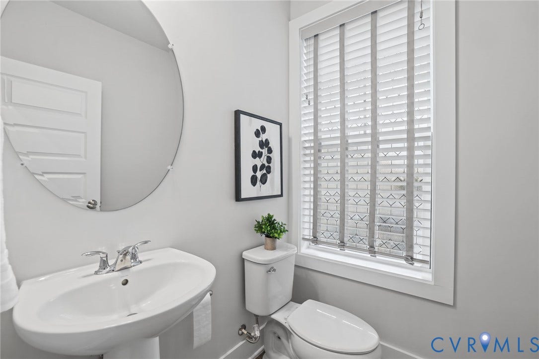 597 Weaver Brook Walk, #B, Richmond, VA 23233 Pedestal sink with polished chrome dual-handle faucet, oval frameless wall mirror, and window with built-in slatted blinds