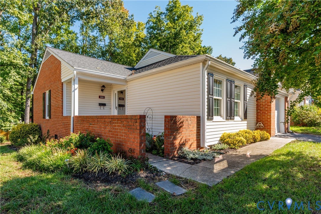Brick and siding exterior with a covered entry, mature landscaping, and a paved walkway