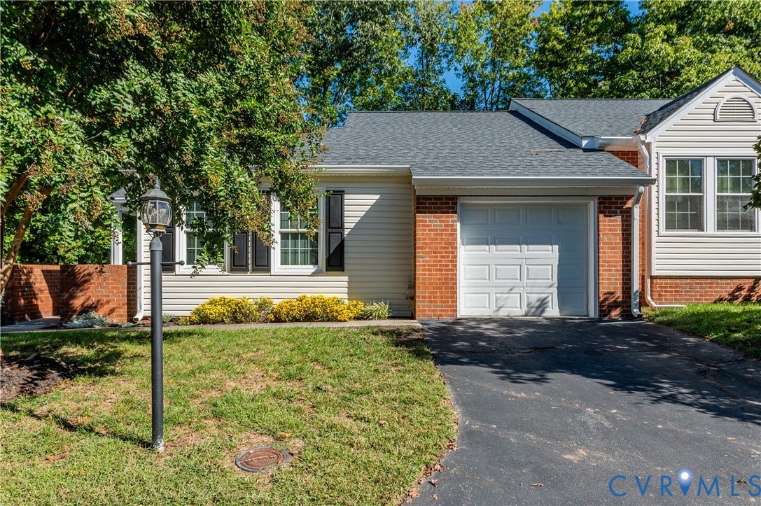 Brick and siding exterior featuring an attached garage, asphalt driveway, and mature landscaping