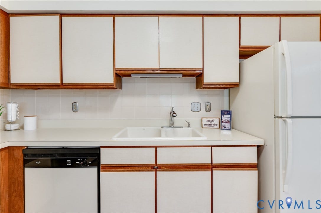 White cabinetry with wood-finish trim, a double basin sink with a chrome faucet, and a white tile backsplash
