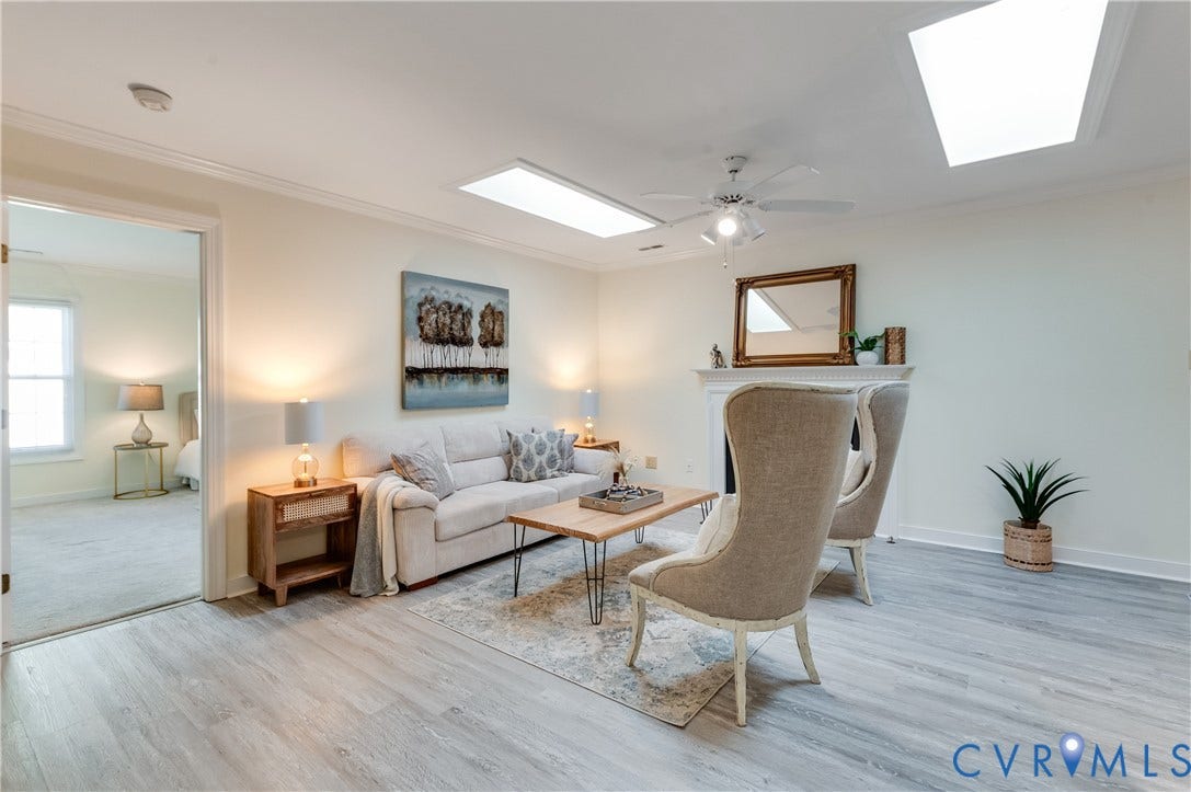 Living space featuring light wood-finish flooring, a ceiling fan, two skylights, and a fireplace with a mantel