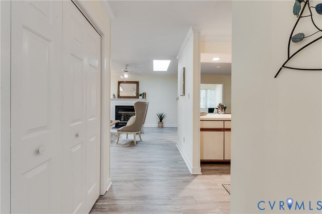 Light wood-finish flooring throughout, white bi-fold closet doors, white fireplace with mantel, recessed lighting, and a skylight