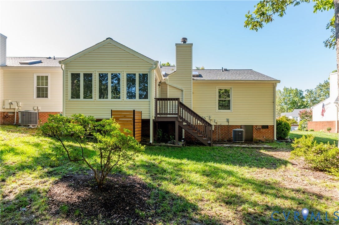 Rear exterior featuring a sunroom addition with multiple windows, an exterior deck with stairs, a brick foundation, and a side chimney