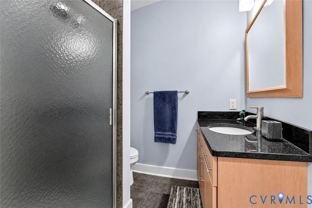 Frosted glass shower enclosure, wood-finish vanity with drawer and cabinet storage, under-mount sink, black stone countertop, and wood-framed mirror