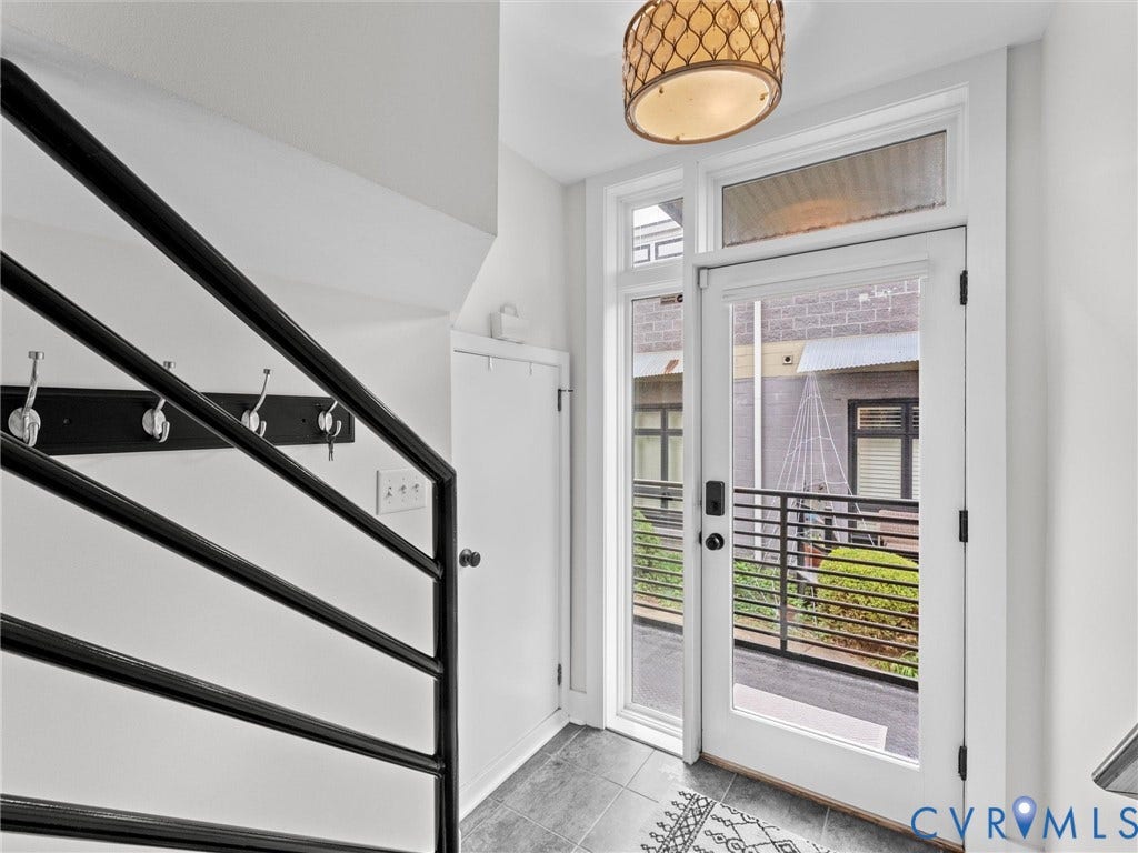 Entryway featuring a full-light door with transom windows, black metal railings, and dark tile flooring