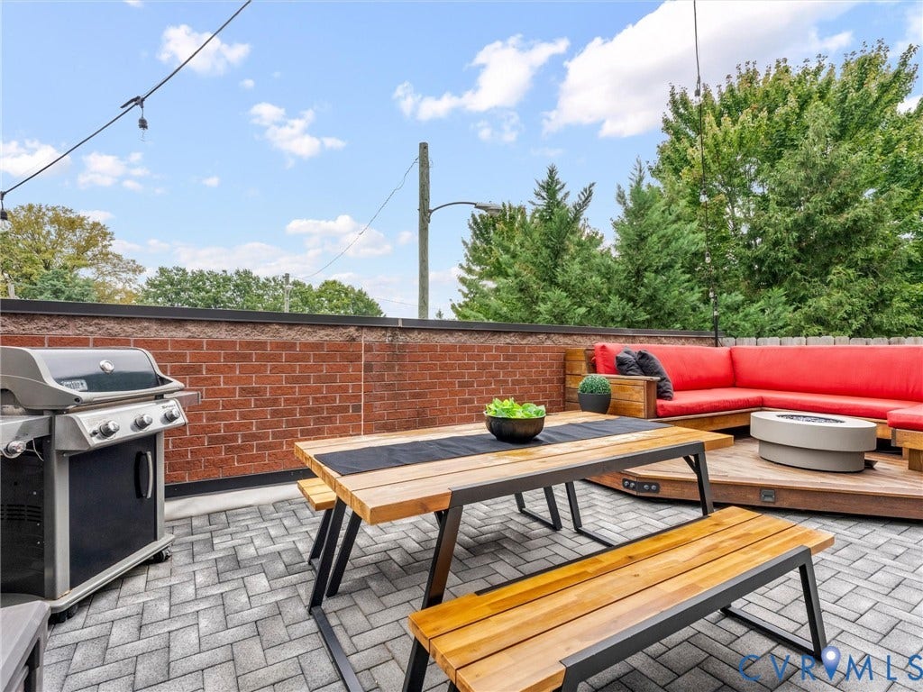Expansive rooftop patio featuring herringbone paver flooring, a brick half-wall, and a built-in wood deck