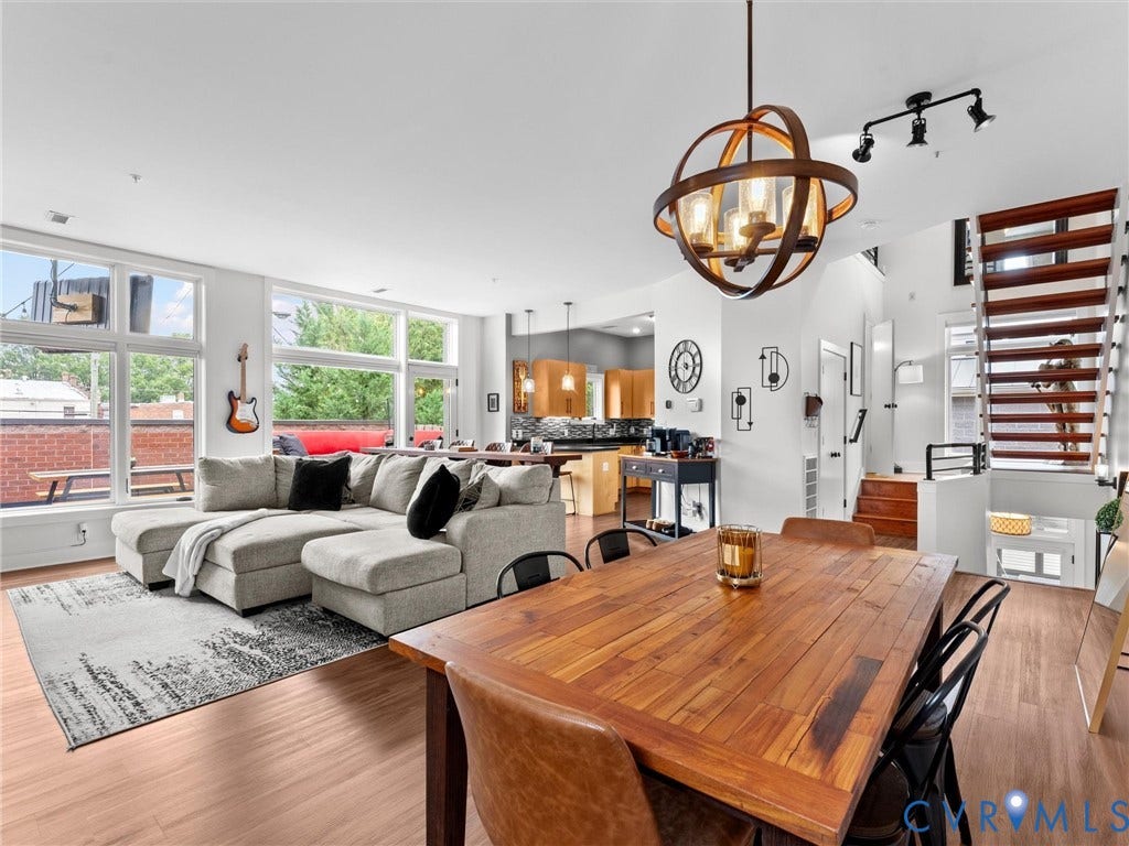 Open-concept living area with abundant natural light from expansive windows, featuring wood-finish flooring and a contemporary orb chandelier