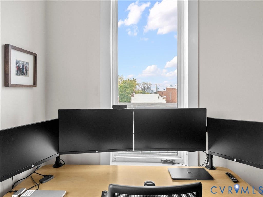 Light-filled interior space featuring a large window, light-toned wall finishes, and wood-finish desk surface