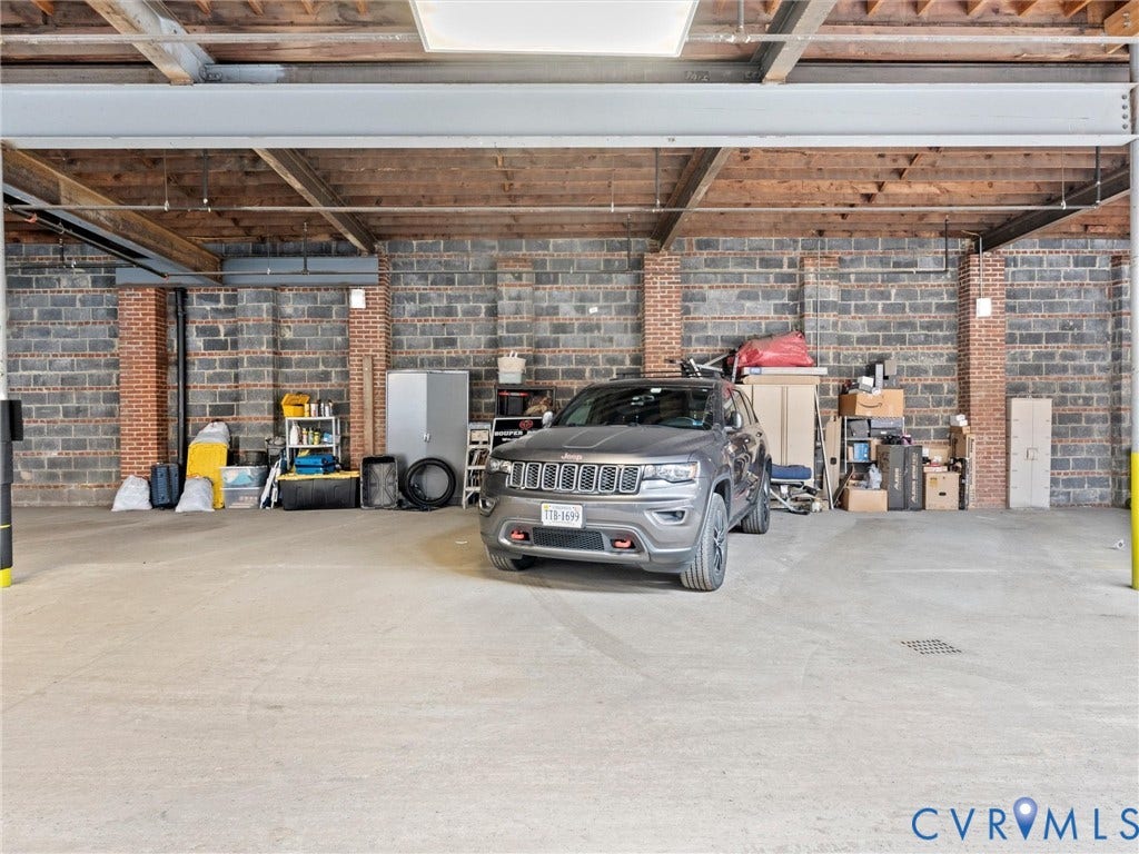 Concrete flooring with exposed ceiling joists, overhead lighting, and brick accent walls