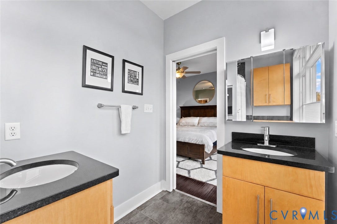 Dual vanity sinks with black countertops, light wood-finish cabinetry, and a mirrored medicine cabinet