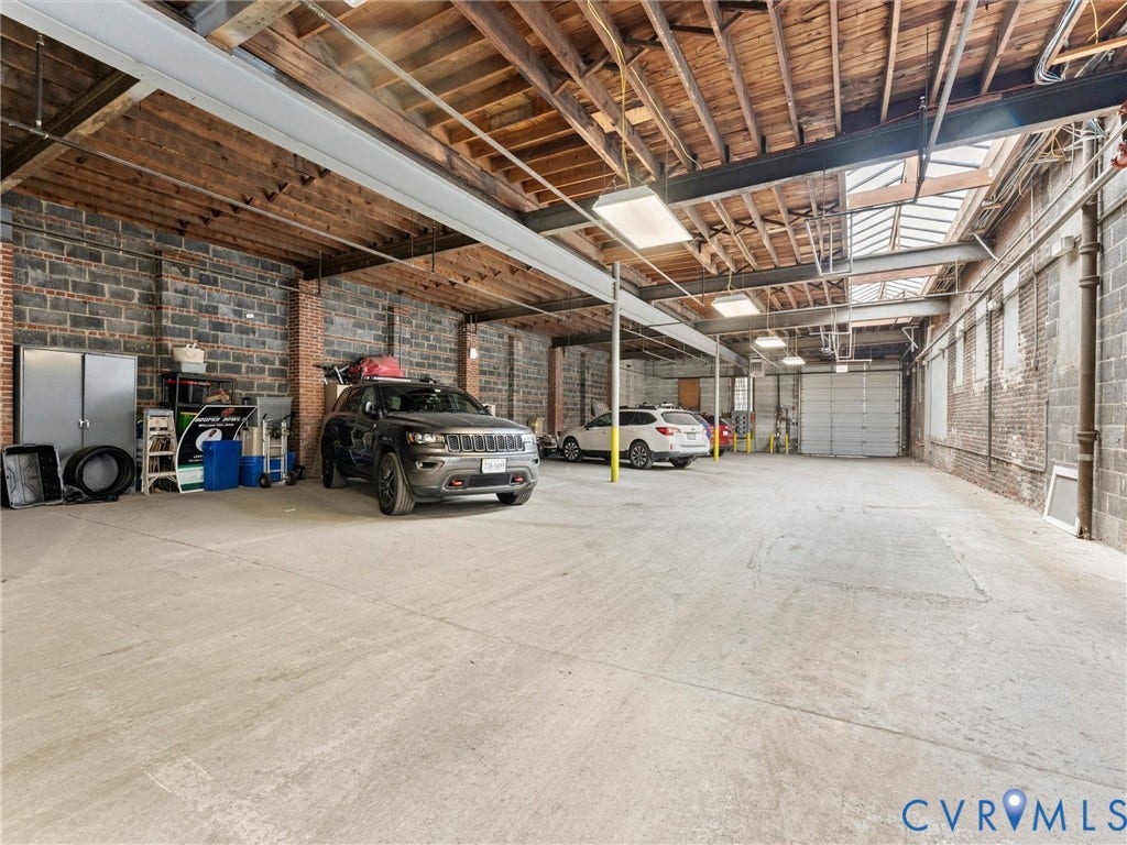 Exposed brick walls, concrete flooring, exposed wood beam ceiling, skylights, and multiple roll-up doors