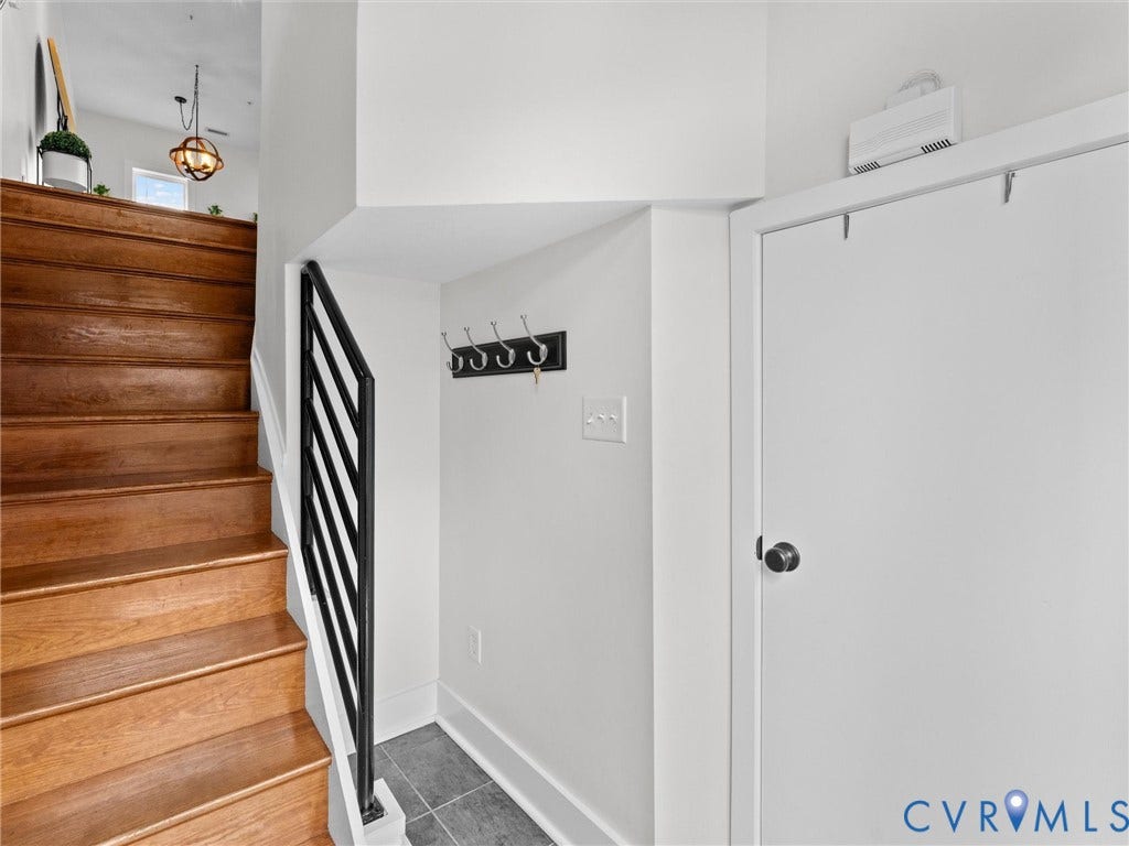 Hardwood staircase with a black metal railing, tiled landing, and a built-in coat rack