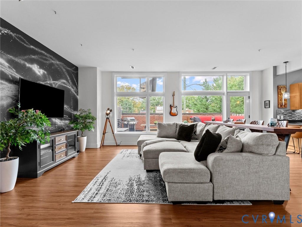 Wood-finish flooring throughout, prominent accent wall, ample natural light from large windows, recessed ceiling lighting, and a built-in media console